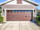 Home's garage has a brown door with decorative windows and exterior carriage lights at 22004 Belgian Ct, Mount Dora, FL 32757