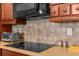 Close-up of a kitchen with light brown cabinets, countertops, a black cooktop, and backsplash in diamond pattern at 1382 Heritage Landings Dr, Lakeland, FL 33805