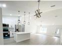 Open-concept kitchen featuring stainless steel appliances, an island, modern pendant lighting, and bright white cabinets at 3245 Se 142Nd Pl, Summerfield, FL 34491