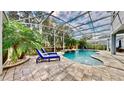 Beautiful screened-in pool area with stone pavers, waterfall feature, lush landscaping, and lounge chairs at 1457 Olympic Club Blvd, Champions Gate, FL 33896