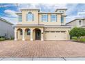 A charming two-story stucco home with a brick driveway and an attached two-car garage and manicured landscaping at 220 Clawson Way, Kissimmee, FL 34747