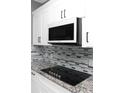 Close up of kitchen showcasing sleek stovetop, modern backsplash, granite countertops, and white cabinets at 1991 Sanderlin Point Loop, Apopka, FL 32703
