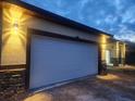 Spacious two-car garage featuring a modern white door and stone accents with outdoor lighting at 13074 Sw 104Th Ln, Dunnellon, FL 34432