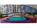 Community pool with lounge chairs and umbrellas next to a high rise building with many windows and red brick accents at 700 Mirror Nw Ter # 403, Winter Haven, FL 33881