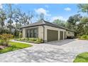 Exterior showcasing a three-car garage with a paved driveway, lush landscaping, and neutral-colored siding at 2337 Legacy Ln, New Smyrna Beach, FL 32168