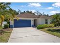 View of a one-story home featuring a bright blue garage door, well-maintained lawn, and lush, vibrant landscaping at 43 Pergola Pl, Ormond Beach, FL 32174