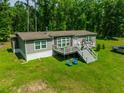 Aerial view of grey home with a deck, white railings, lush green grass, and surrounding mature trees at 21375 Nw 150Th Avenue Rd, Micanopy, FL 32667