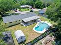 Aerial view of a home's backyard with a pool, covered patio, storage shed, and fenced yard surrounded by mature trees at 1505 Valencia Ave, Daytona Beach, FL 32117