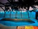 Inviting screened-in pool illuminated with colorful lights against lush landscaping at night at 1786 Red Clover Ln, The Villages, FL 32163