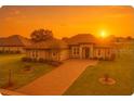 Inviting single-story home featuring a well-manicured lawn, brick driveway, and beautiful landscaping at sunset at 5159 Greens Dr, Lady Lake, FL 32159