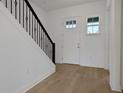 Bright foyer with light hardwood floors, a white door, and a staircase with a black metal railing at 6608 Quest St, St Cloud, FL 34771