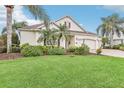 Tan two-story house with a two-car garage, palm trees, and lush landscaping at 1596 Birmingham Ter, The Villages, FL 32162