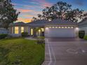 Inviting home with a two-car garage, manicured lawn, and mature landscaping under a colorful evening sky at 8288 Se 177Th Winterthur Loop, The Villages, FL 32162