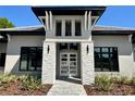 Close-up of a modern home's entrance with stone pillars, a glass door, and manicured landscaping at 16914 Vinci Way, Bella Collina, FL 34756
