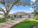 Charming single-story home with a long, patterned driveway, lush green lawn, and mature trees, and a two car garage at 11584 Se 175Th St, Summerfield, FL 34491
