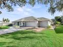 Single-story home with a two-car garage, lush green lawn, and well-maintained landscaping and large mature trees at 11584 Se 175Th St, Summerfield, FL 34491