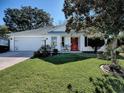 White house with red door, two-car garage, and well-manicured lawn at 17242 Se 94Th Coults Cir, The Villages, FL 32162