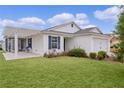 White house with blue shutters, covered patio, and lush green lawn at 3707 Gravel Ct, The Villages, FL 32163