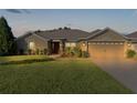 Tan one-story house with a red door, two-car garage, and lush green lawn at dusk at 9800 Pepper Tree Trl, Wildwood, FL 34785