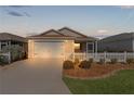 Tan house with white picket fence, two-car garage, and screened porch at dusk at 1387 Zest Ave, The Villages, FL 32163