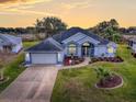 Single-story home with gray roof, white walls, and landscaped yard at sunset at 5626 Squires Dr, Leesburg, FL 34748