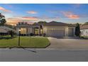 Tan house with a three-car garage, lush landscaping, and a beautiful sunset at 9565 Se 124Th Loop, Summerfield, FL 34491