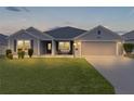 Gray one-story house with a two-car garage and well-manicured lawn at dusk at 11414 Roma Rd, Oxford, FL 34484