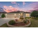 Tan house with landscaped yard, 3-car garage, and paver driveway at sunset at 2096 Odessa Cir, The Villages, FL 32162