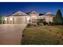 Well-lit home exterior at night showcasing a two-car garage and landscaping at 3590 Ithaca Ter, The Villages, FL 32163