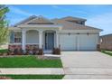Charming home featuring a two-car garage, covered entryway with columns, stone accents, and freshly manicured lawn at 5119 Firebush Dr, Apopka, FL 32712