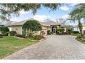 Charming single-story home features a manicured lawn, lush landscaping, and a brick driveway leading to an attached garage at 6216 Landings Blvd, Lady Lake, FL 32159