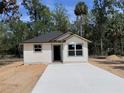 Newly constructed home with light siding, a dark roof, and a fresh concrete driveway against a natural backdrop at Lot 42 Indian Estates Cr 423, Lake Panasoffkee, FL 33538