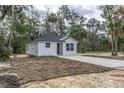 Charming new construction home with black roof, white siding, and driveway, nestled among mature trees at Lot 42 Indian Estates Cr 423, Lake Panasoffkee, FL 33538