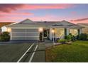 White house with green shutters, landscaped lawn, and a two-car garage at dusk at 16967 Se 93Rd Cuthbert Cir, The Villages, FL 32162