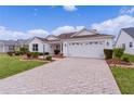 Front view of a white house with a paver driveway and nicely landscaped yard at 1216 Addison Ave, The Villages, FL 32162