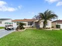 Well-maintained single-story home with lush green lawn, a golf cart, and tropical landscaping at 17412 Se 76Th Flintlock Ter, The Villages, FL 32162