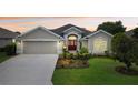 Charming single-story home featuring a manicured lawn, mature landscaping, and a welcoming red front door at 584 Bradford Loop, The Villages, FL 32163