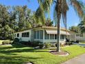 Tan mobile home with corner lot, lush landscaping, and palm trees at 114 Chestnut St, Leesburg, FL 34748