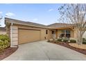 Tan single story home with attached garage and mature landscaping in front and rocking chairs on the front porch at 1941 Loadstar Ave, The Villages, FL 32162