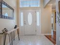 Bright foyer features a white front door with decorative glass, neutral tile flooring, and a stylish accent table at 320 Rhapsody Path, The Villages, FL 32162