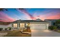 Charming single-story home featuring a well-manicured front yard and attached two-car garage at dusk at 1555 Ward Ct, The Villages, FL 32162