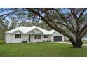 White farmhouse exterior with metal roof, landscaping, and large tree at 18315 Dells Cv, Groveland, FL 34736