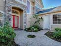 Inviting entryway with stone accents, red front door, complemented by lush landscaping and a brick paver walkway at 16126 Bristol Lake Cir, Orlando, FL 32828