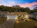 Charming single-story home with a stone driveway, well-manicured lawn, and beautiful landscaping at dusk at 2010 Harston Trl, The Villages, FL 32162