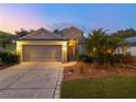 Inviting home exterior featuring a two-car garage, illuminated entryway, and lush landscaping, captured during twilight at 235 Pima Trl, Groveland, FL 34736