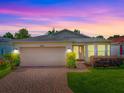 Attractive single-story home with two-car garage, brick driveway, and lush front lawn at twilight at 32708 Westwood Loop, Leesburg, FL 34748