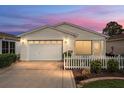 Charming home exterior showcasing a white picket fence, manicured lawn, and attached garage at dusk at 2277 Whisper St, The Villages, FL 32162