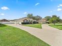 Single-story home featuring a long driveway, manicured lawn, vibrant blue shutters, and a two-car garage at 10230 Barrington Ct, Leesburg, FL 34788