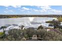 Breathtaking aerial view of a home with a shimmering lake backdrop, surrounded by lush greenery and blue skies at 10606 Masters Dr, Clermont, FL 34711