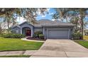 Inviting single-story home showcasing lush landscaping, a two-car garage, and an attractive red front door at 10606 Masters Dr, Clermont, FL 34711